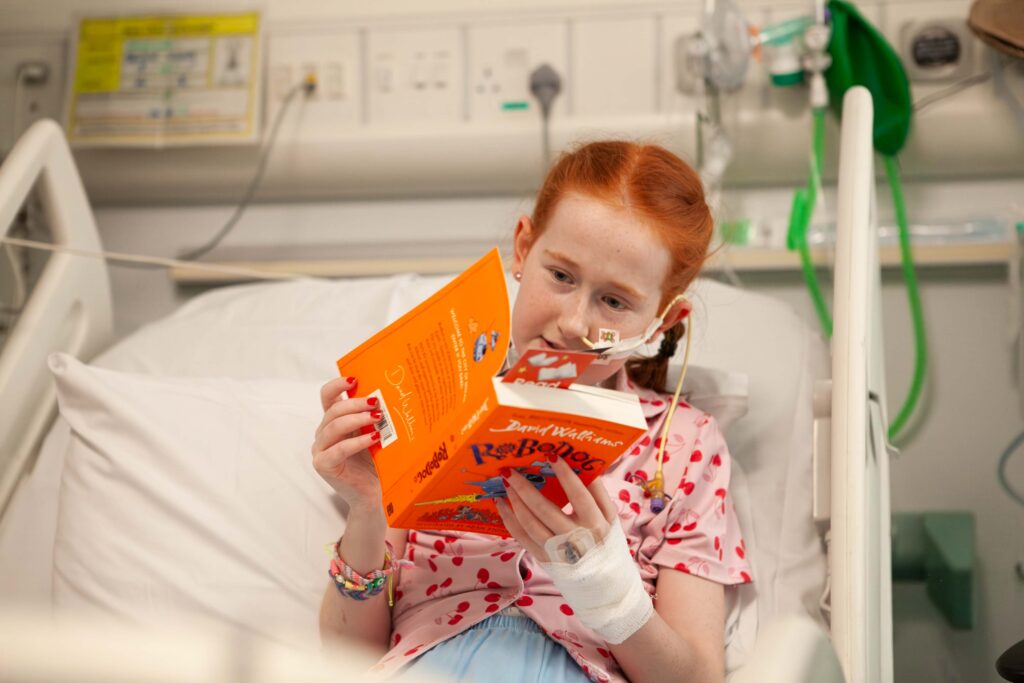 A girl in a hospital bed with a book reading