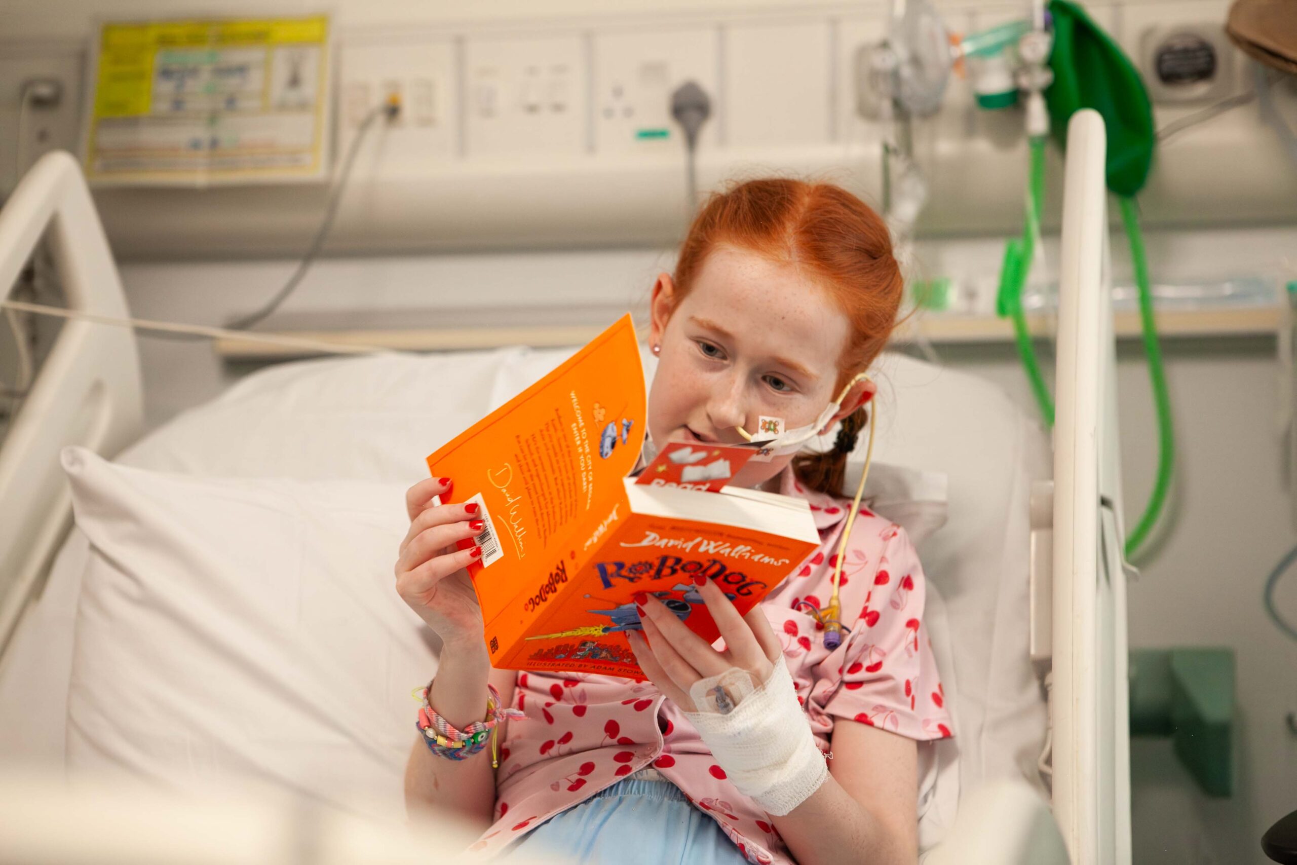 A girl in a hospital bed with a book reading