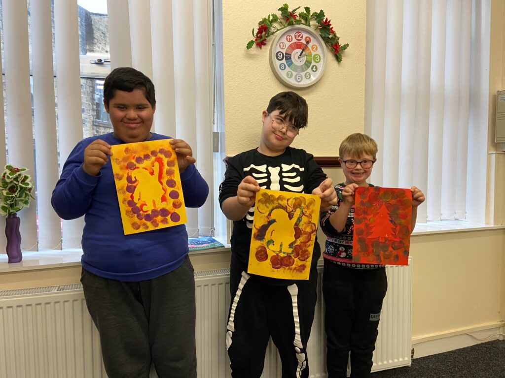 Three young people hold up autumn artwork