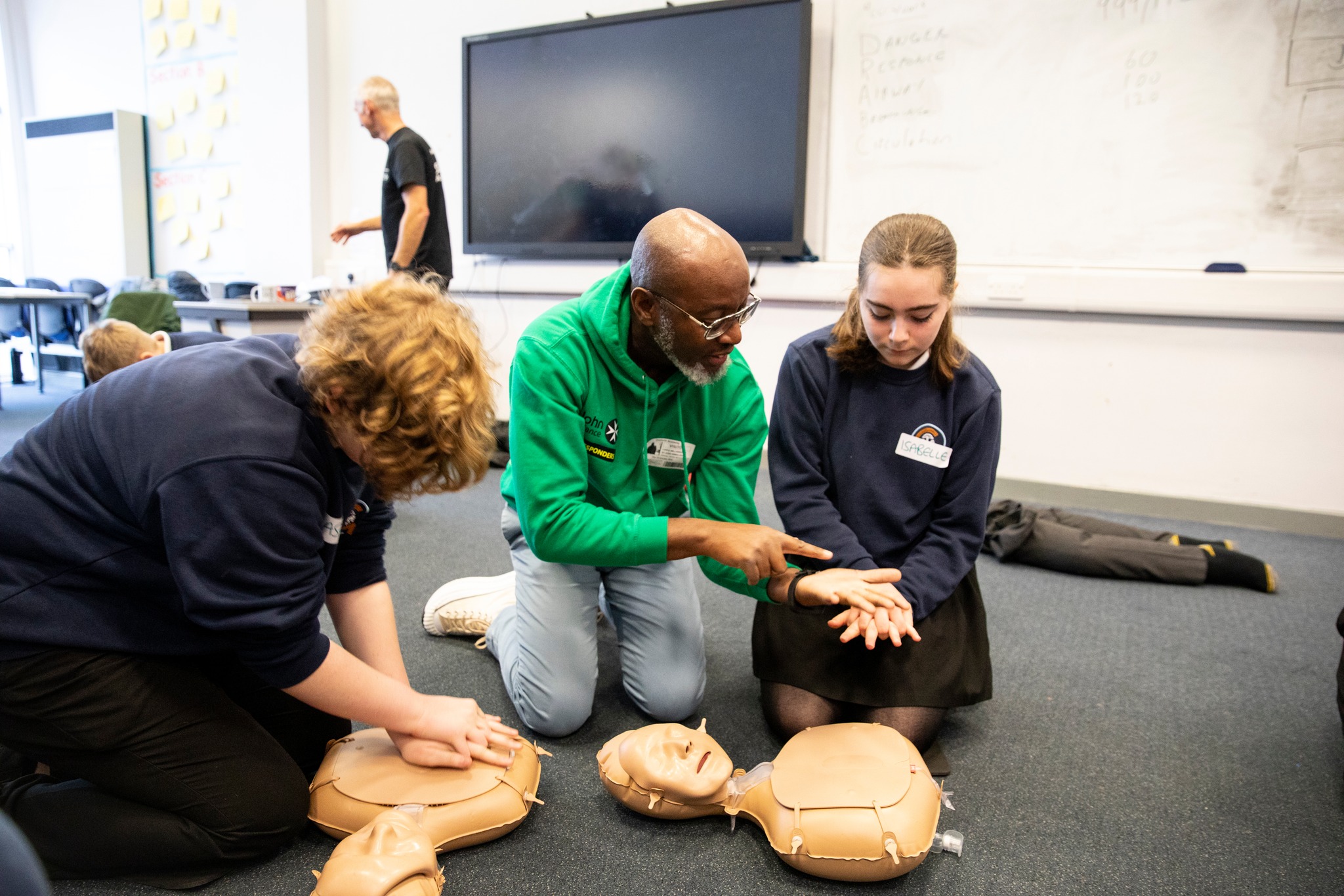 An adult in a green top shows two young responders how to perform cpr.