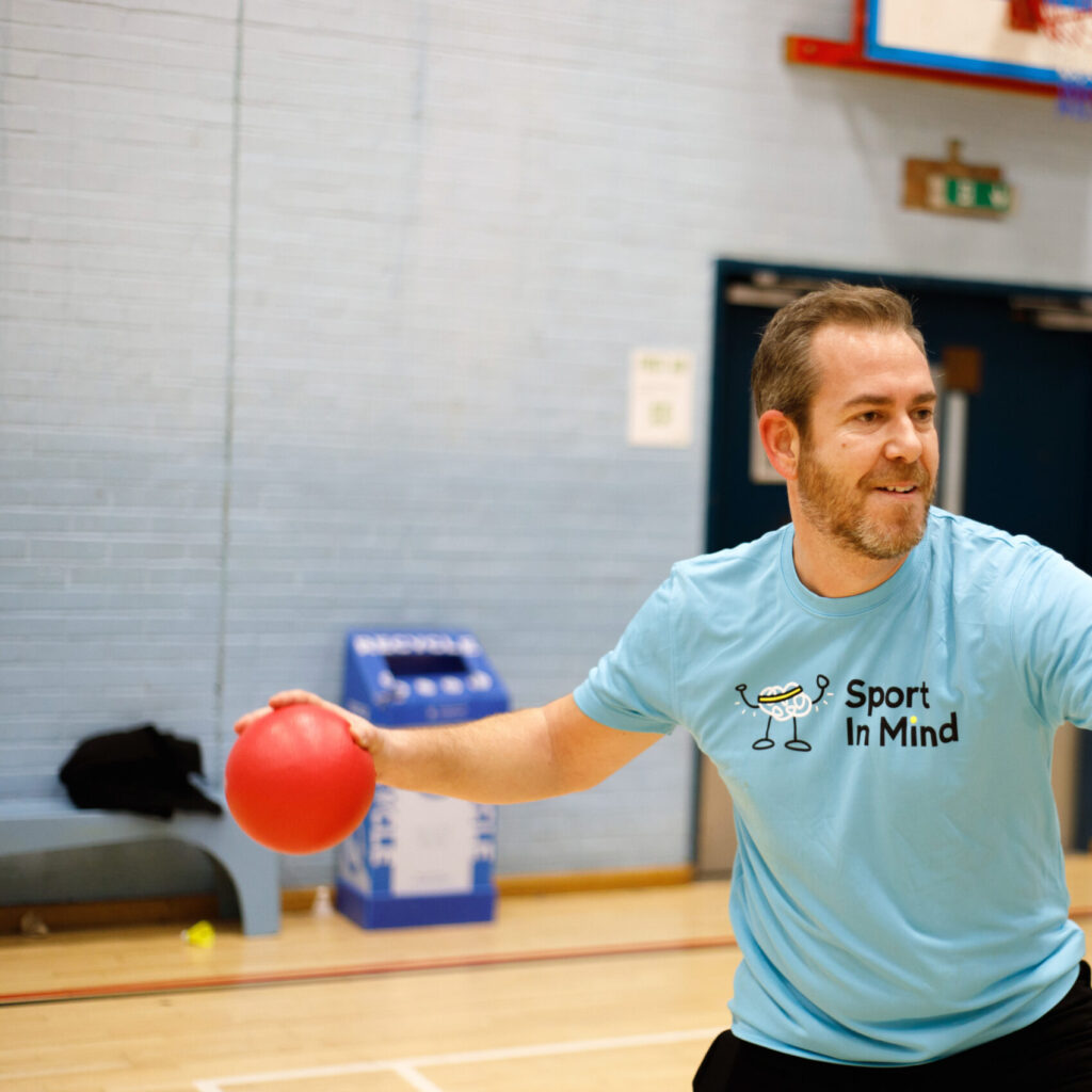 A man plays table tennis in a blue Sport in Mind t-shirt