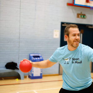 A man plays table tennis in a blue Sport in Mind t-shirt