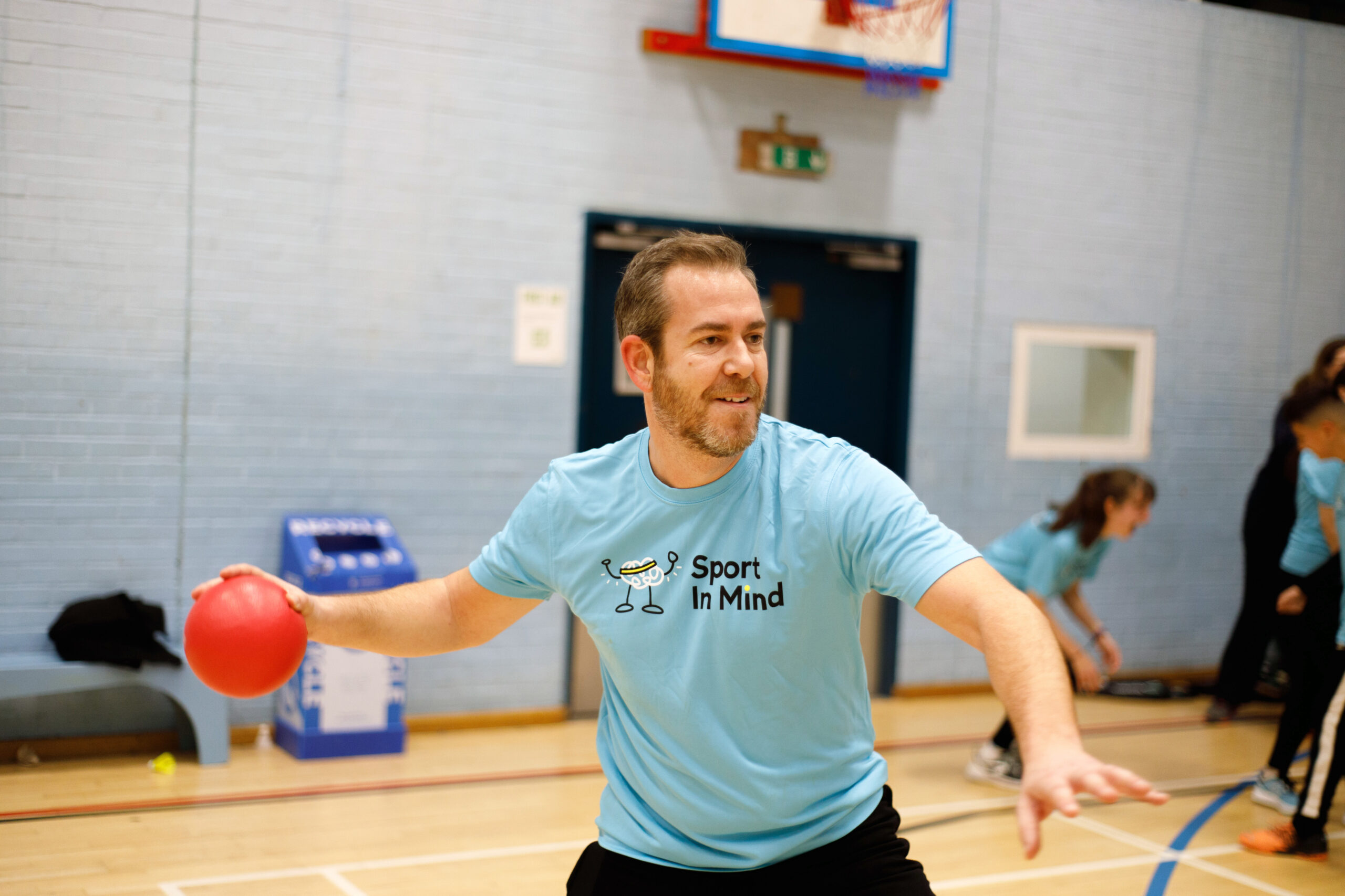 A man plays table tennis in a blue Sport in Mind t-shirt