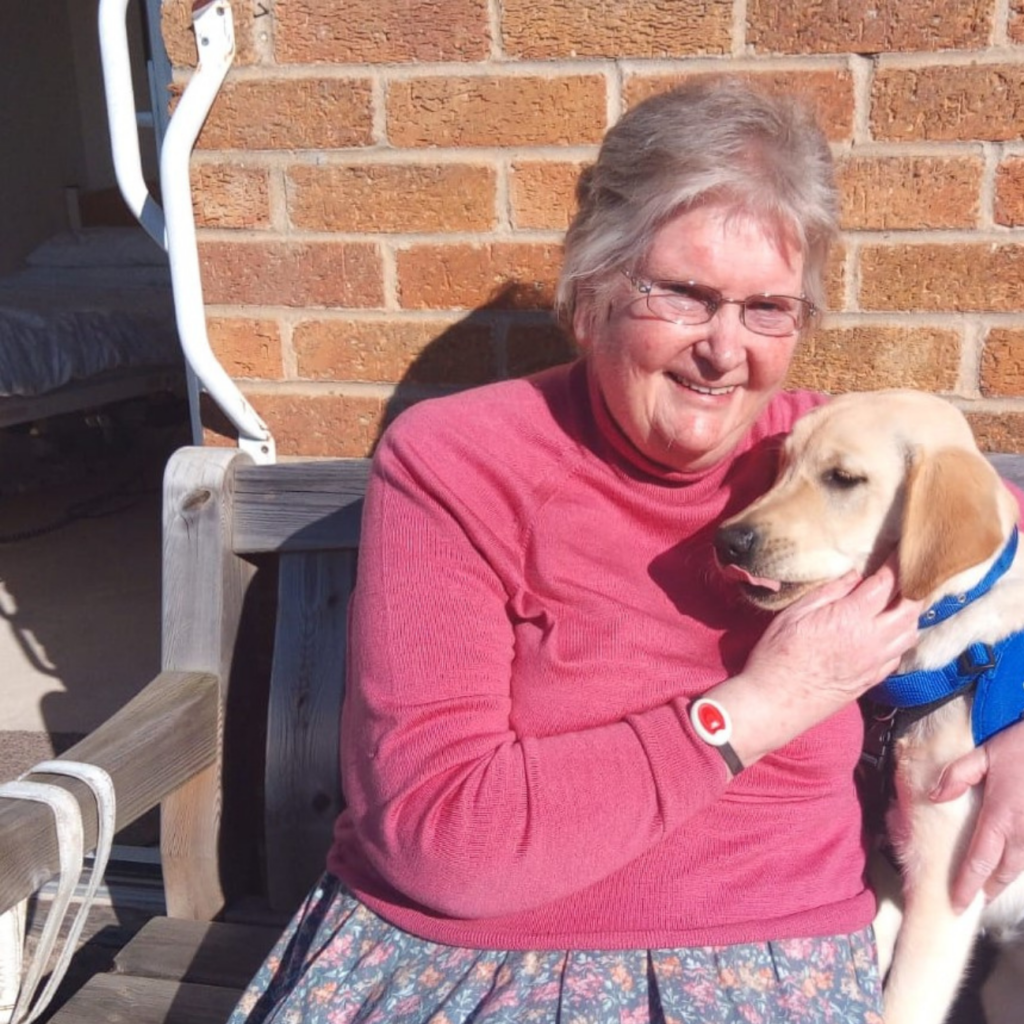 A lady and a dog sit in front of a brick wall