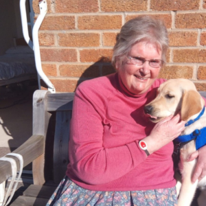 A lady and a dog sit in front of a brick wall