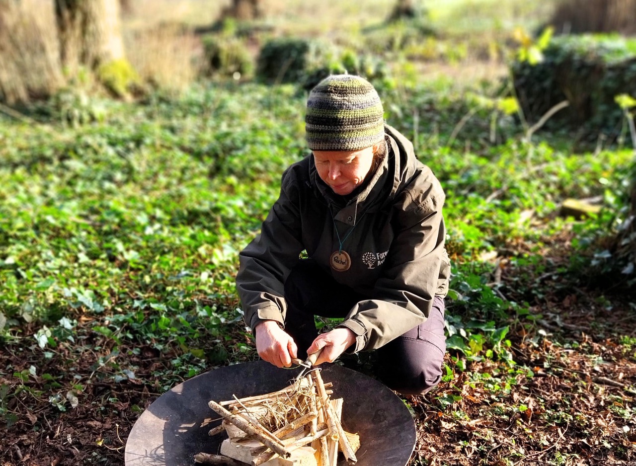 a man whittles a stick in a forest clearing