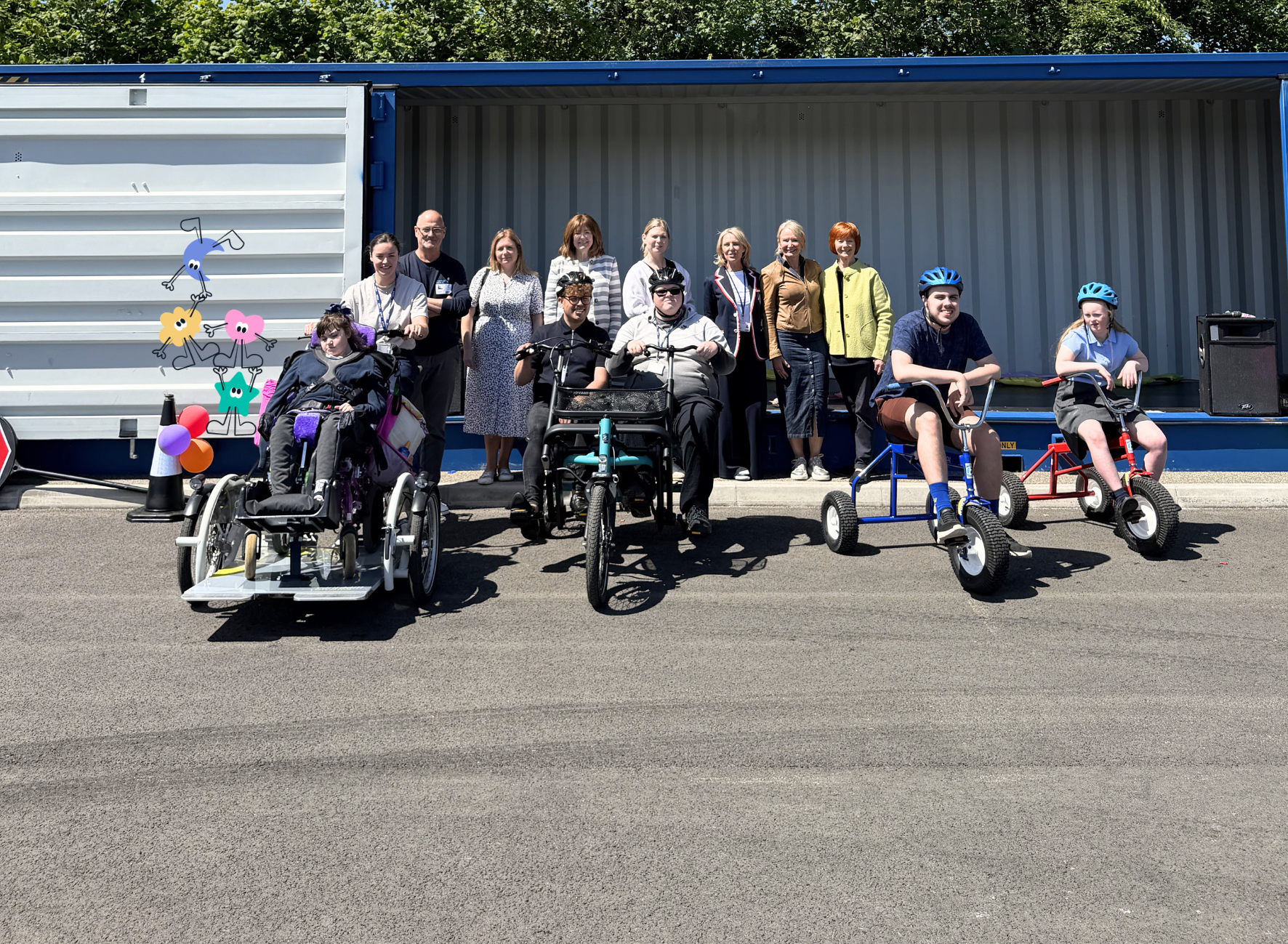 A group of people on a yard with some adaptable trikes and cartoon characters in the background