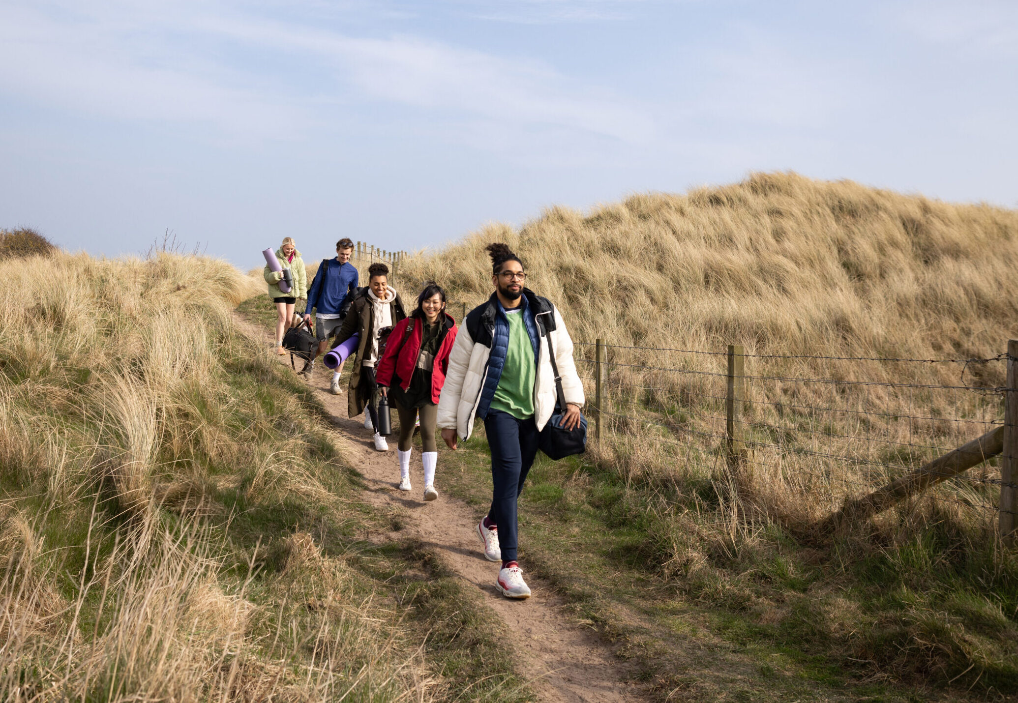 A group of people walk down a sand dune on to a beach in Norfolk